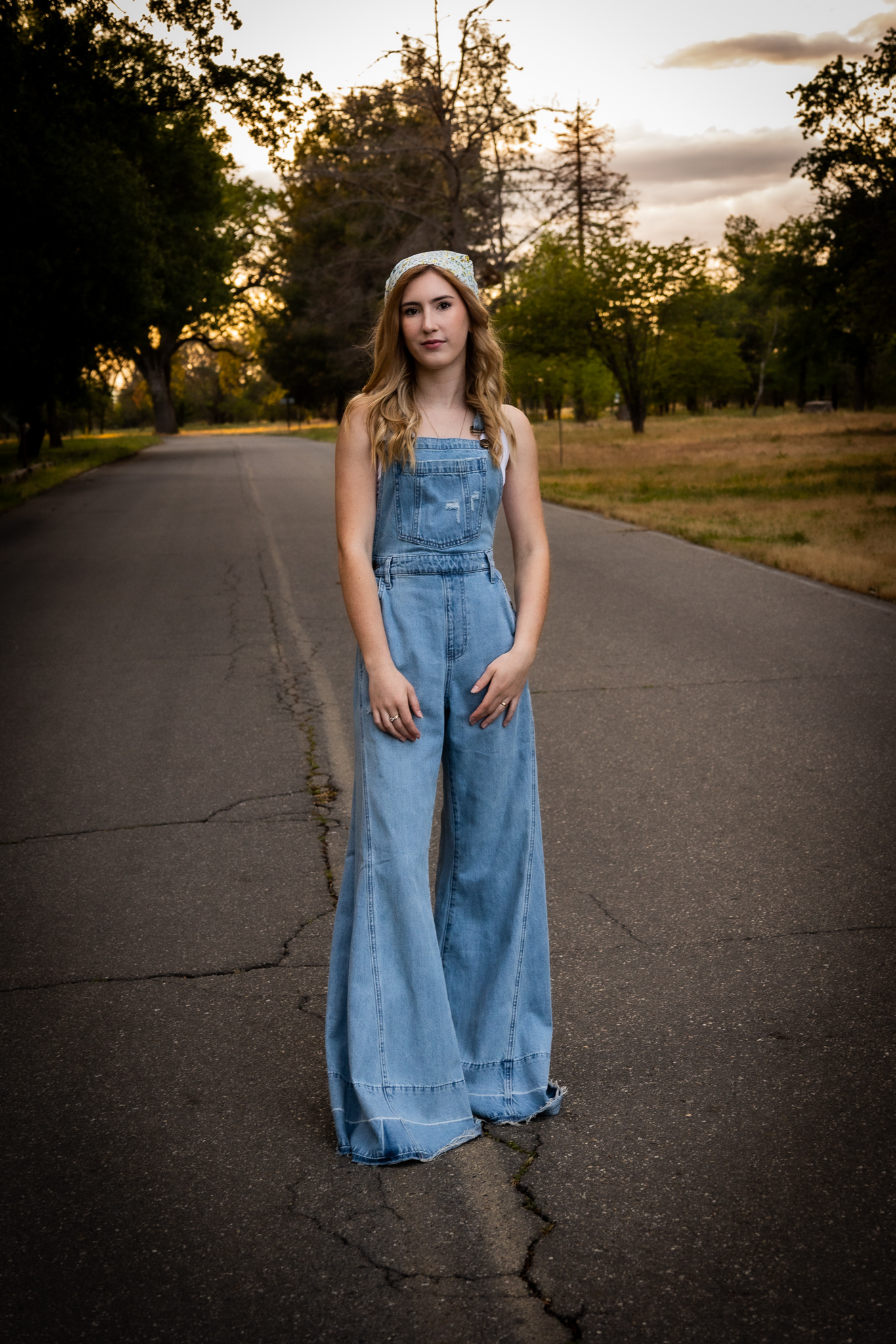 girl wearing bell bottom overalls standing in road during senior session