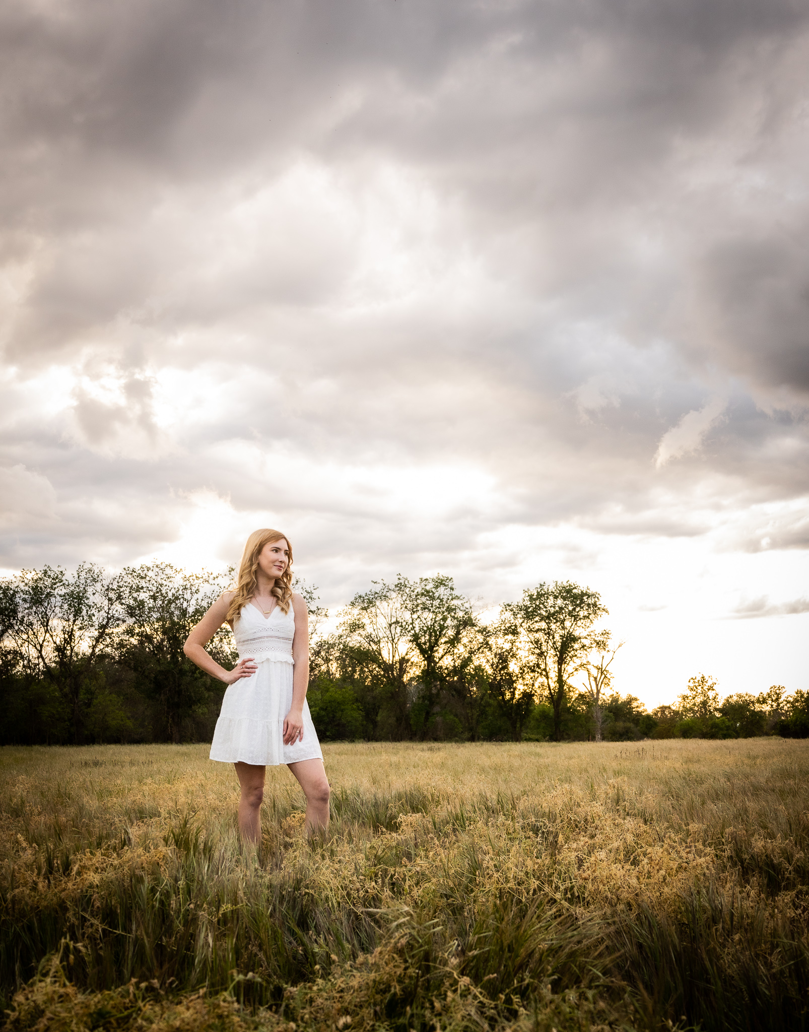girl standing in field with grey clouds during senior session