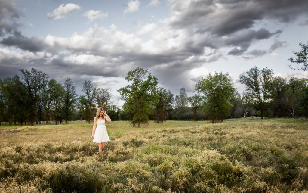 girl in white dress during senior session walking though red bluff field