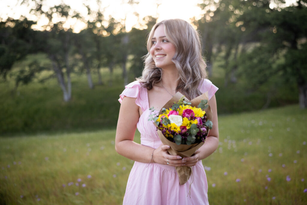 girl holding flowers in field wearing a pink dress