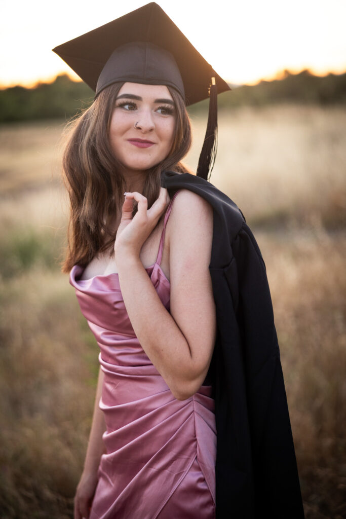 girl looking over her shoulder wearing cap and gown for for graduation
