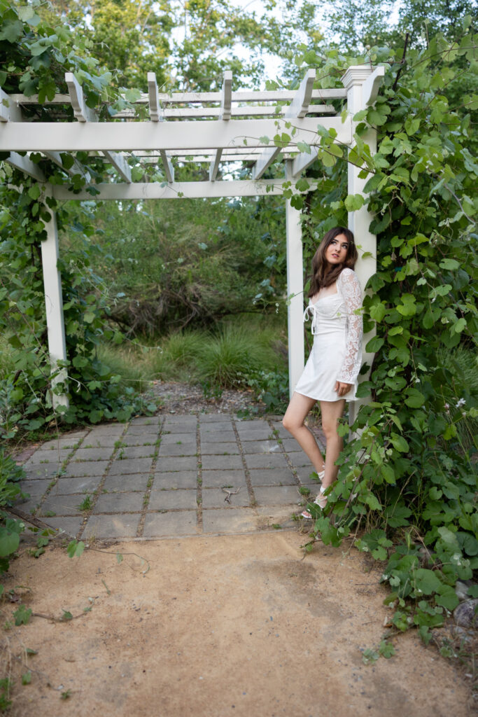 girl in white dress leaning against grape arbor