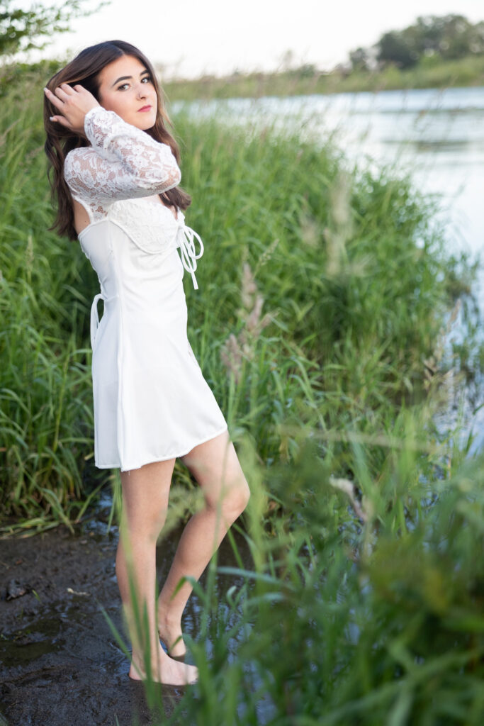 girl brushing hair from her face standing by water